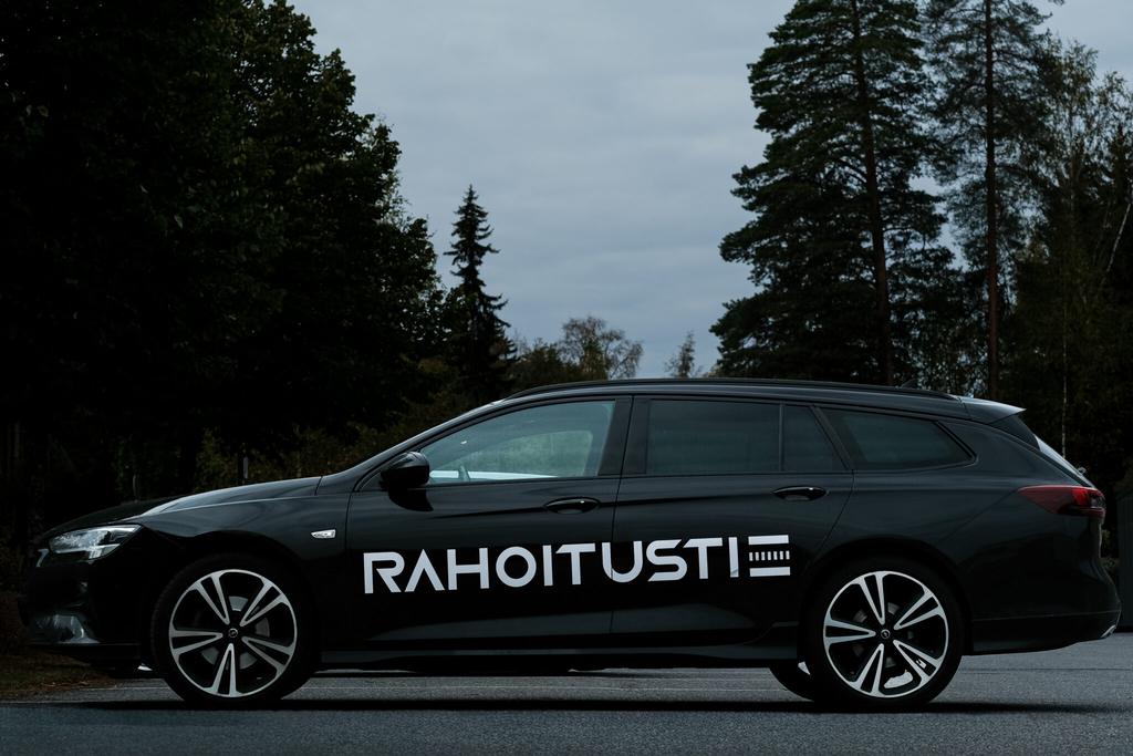 Rahoitustien musta farmariauto iltahämärässä mäntymetsän edessä