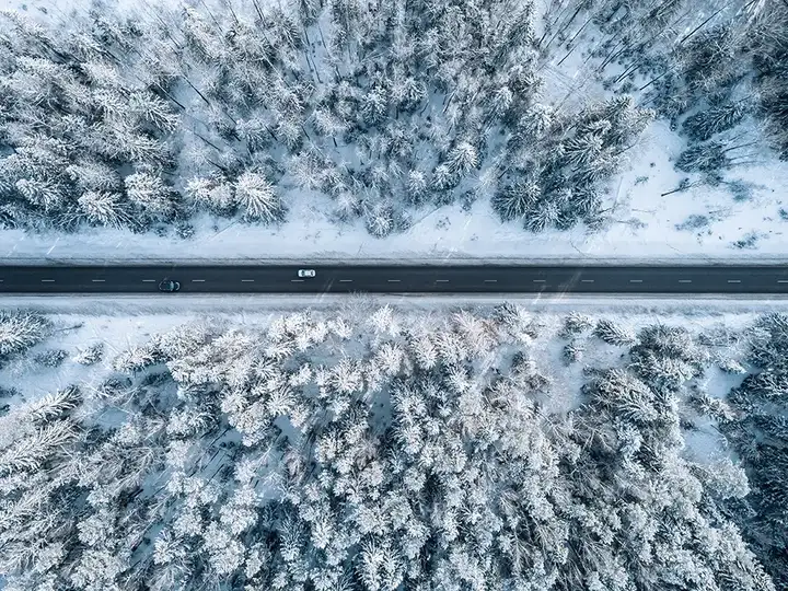Talvinen tie lumisen havumetsän halki ilmasta kuvattuna